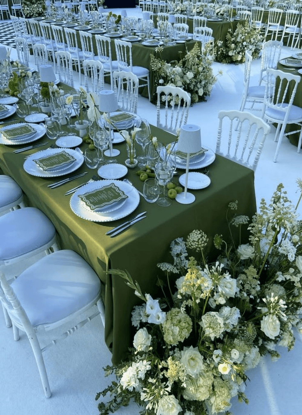 A long banquet table dressed with an olive runner, white florals and full glassware