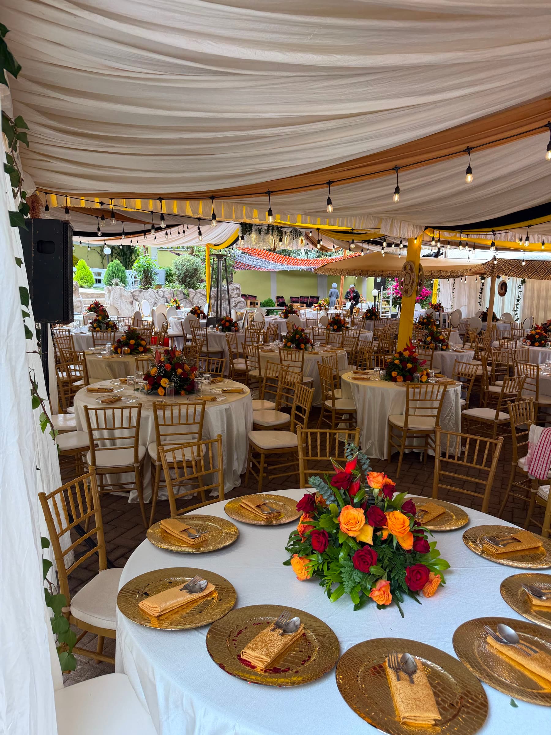 Gold chargers, folded napkins and a centerpiece of red and orange roses on a white tablecloth