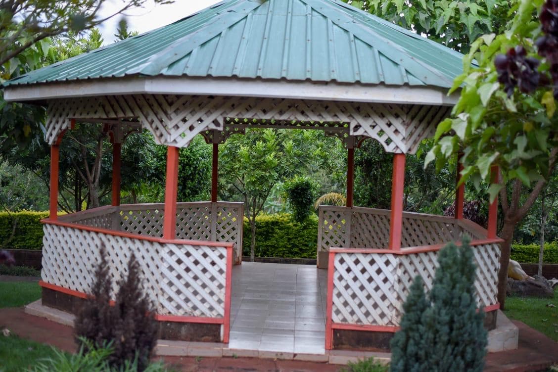 A white lattice gazebo with a green roof among the trees